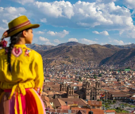 A woman in traditional clothing gazes at the stunning Cusco skyline, capturing Peru's cultural essence.