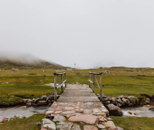 A serene footbridge crossing a stream in the misty countryside of Cusco, Peru.