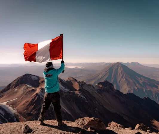 A climber waves the Peruvian flag on a mountain peak with a breathtaking view of the Andes.